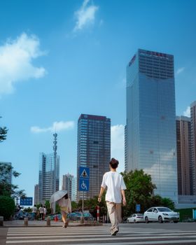 Pedestrians crossing a busy street amid towering skyscrapers on a clear day.