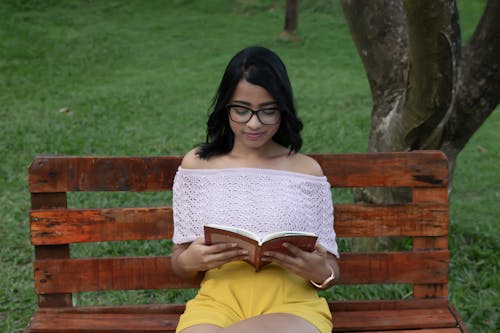 나무 벤치에 앉아있는 동안 책을 읽는 여자