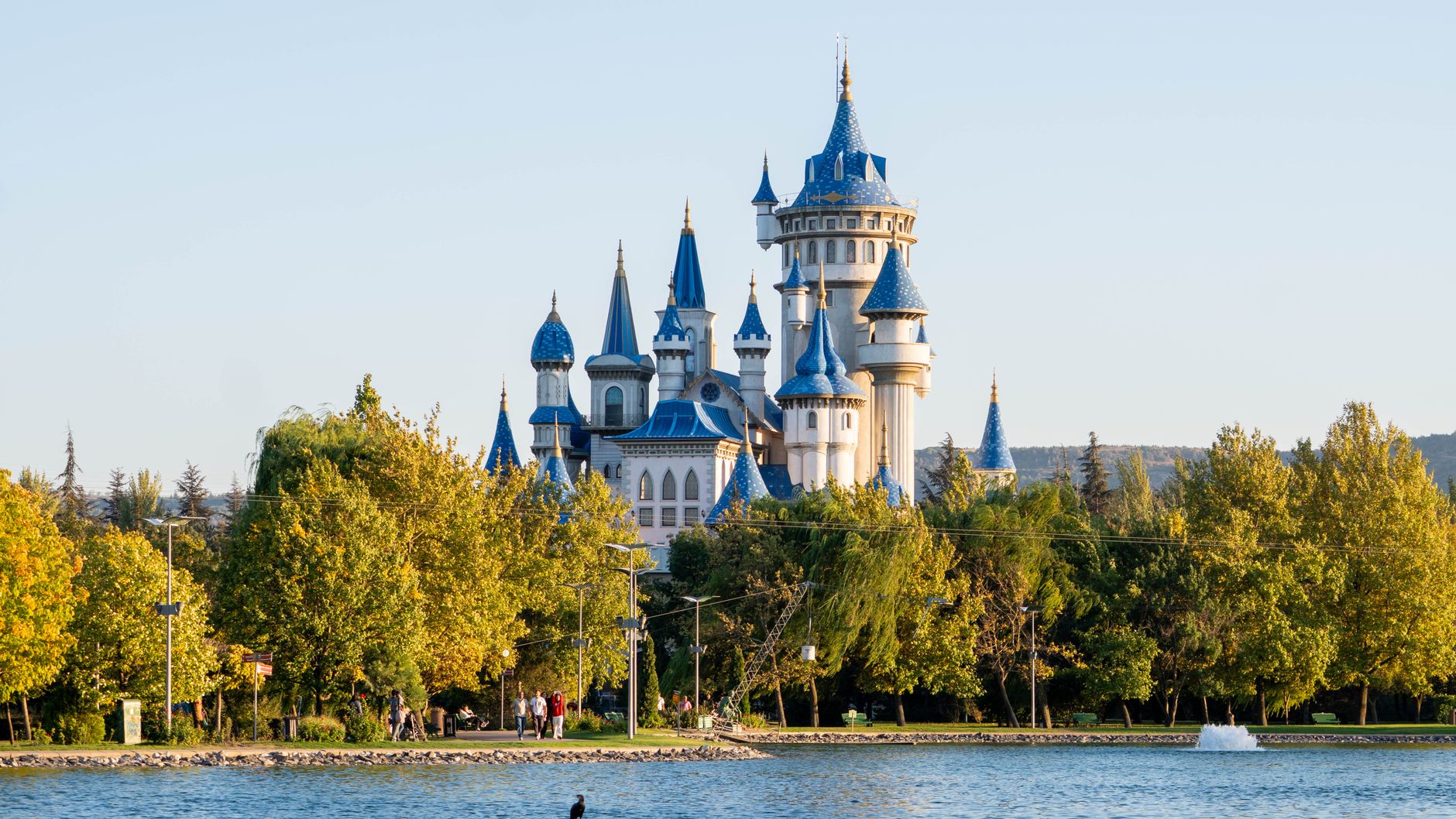 Enchanting fairytale castle with blue spires surrounded by lush trees and a tranquil lake. — free online jigsaw puzzle on JigsawPuzzlesFreeOnline.org
