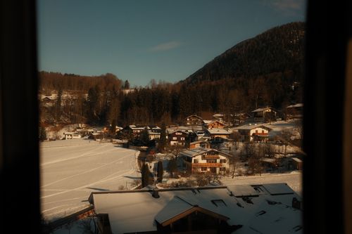 Free Charming village view with snow-covered houses and forested hills in Alpine region at sunset. Stock Photo