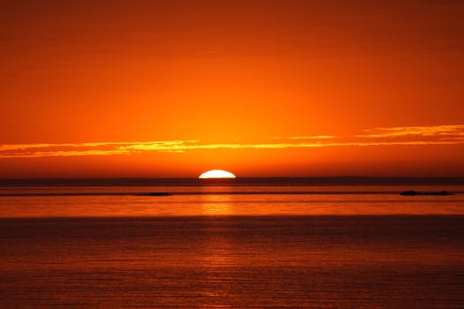 Vibrant orange sunset casting reflections over the tranquil ocean surface.