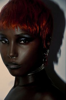 Striking portrait of a woman with dark skin, red hair, and metallic accessories.