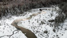 从鸟瞰视角看去，冰封的河流蜿蜒穿过白雪皑皑的冬季景观与茂密的森林