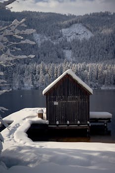 A serene snow-covered cabin by a lake in Austria during winter.