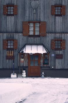 Charming wooden building facade with snowman in front, capturing winter in Austria.