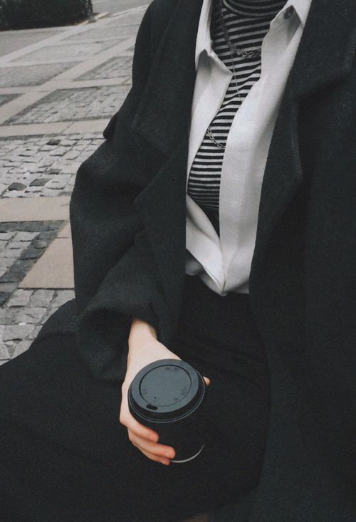 Free Close-up of a woman in a black coat holding a coffee cup outdoors on a fall day. Stock Photo
