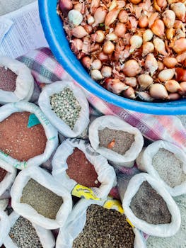 Variety of seeds and fresh onions on display at a vibrant outdoor market stall.