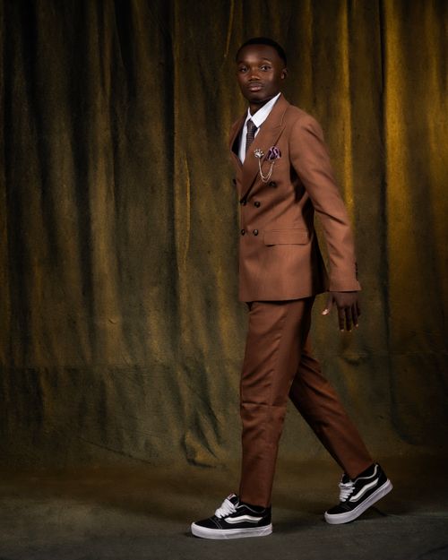 Free Man confidently walking in a brown suit and sneakers, indoor setting. Stock Photo