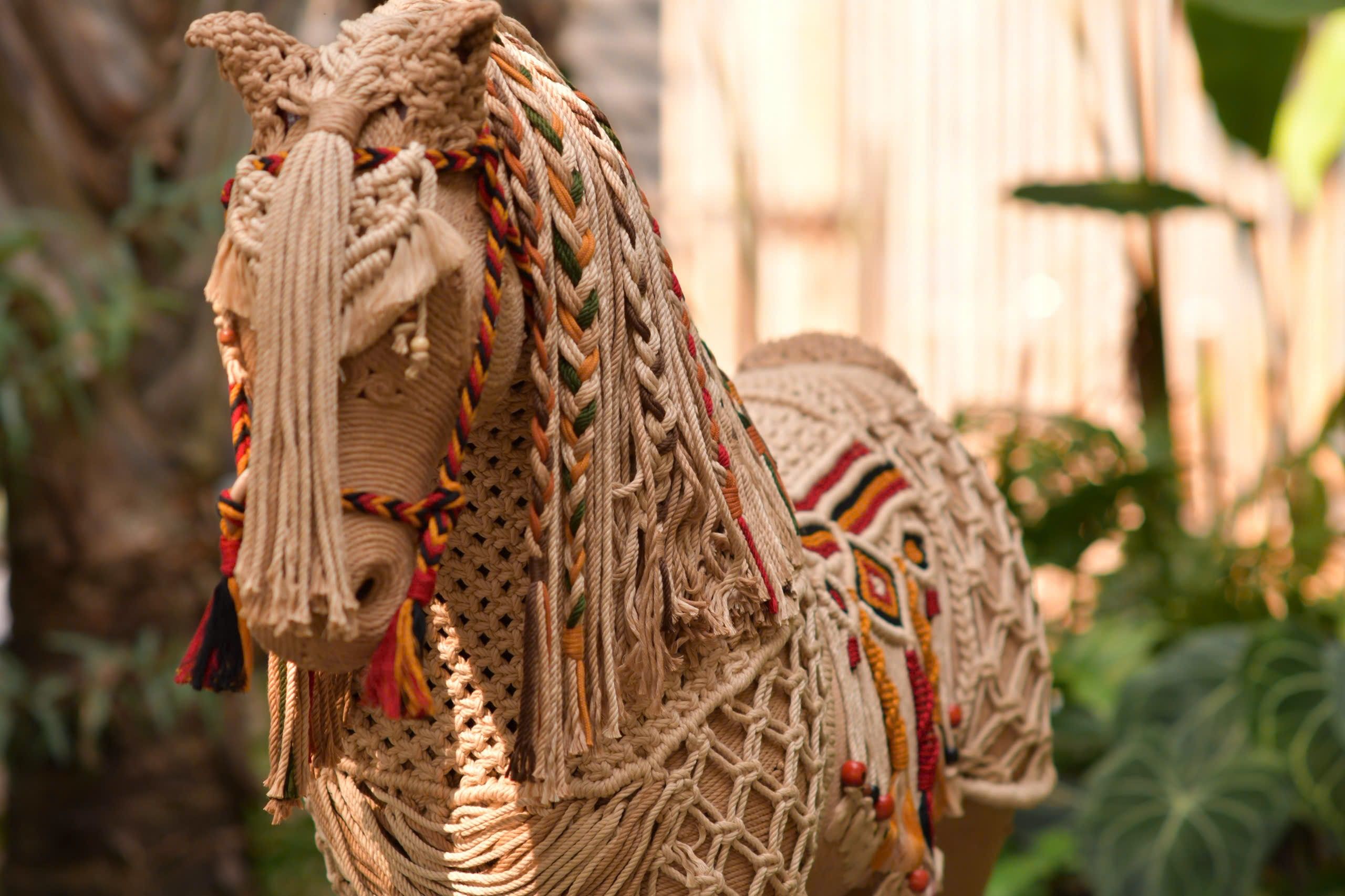 Detailed macrame horse sculpture displayed outdoors with natural greenery.