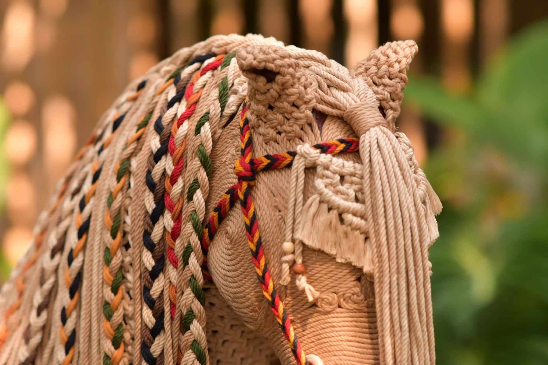 Intricate macramé horse head art featuring colorful braided ropes in a natural setting.
