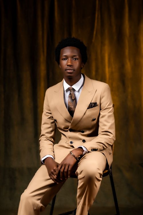 Free A stylish man in a tan suit seated elegantly against a textured backdrop. Stock Photo