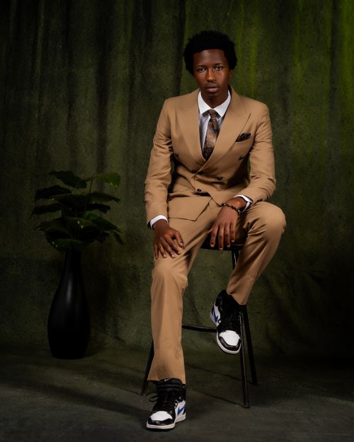Free Elegant man in tan suit and sneakers seated against dark backdrop Stock Photo