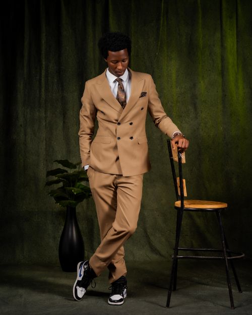 Free A dapper man in a tan suit poses elegantly by a chair indoors against a green backdrop. Stock Photo