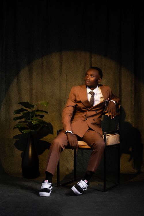 Free Elegant man in a brown suit sitting on chair confidently in a dramatic, modern setting. Stock Photo