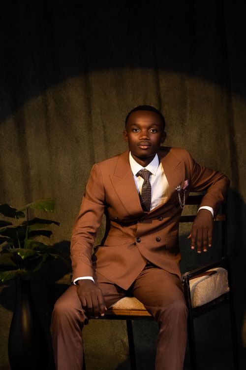 Free Professional portrait of a man in a brown suit seated with a plant and dark background. Stock Photo