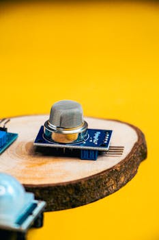 High-quality image of an electronic sensor placed on a round wooden base, contrasting with a vibrant yellow background.