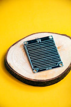 A black sensor module displayed on a wooden slice with a vibrant yellow background.