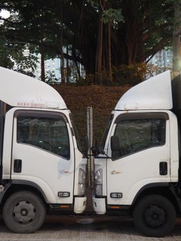 Two symmetrical white trucks parked opposite each other in a Hong Kong street, creating a mirrored urban scene.