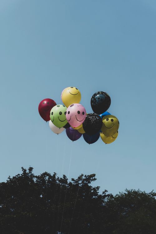 Free Brightly colored smiley face balloons floating against a clear blue sky, evoking joy and celebration. Stock Photo