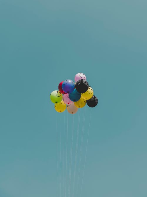 Free Vibrant helium balloons soar against a bright blue sky, evoking joy and celebration. Stock Photo