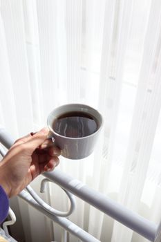 A hand holding a coffee cup near a sunlit window, creating a cozy morning vibe.