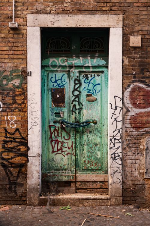 Free A weathered green door covered in vibrant graffiti, set in a rustic brick wall. Stock Photo