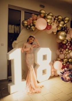 Stunning young woman poses at an 18th birthday celebration with a decorative balloon arch.