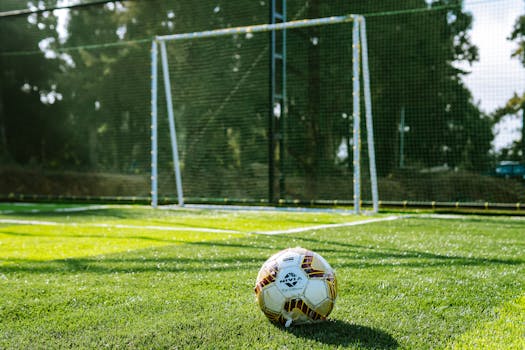 Close-up of a soccer ball on a grass field with a goalpost in the background, outdoor setting.