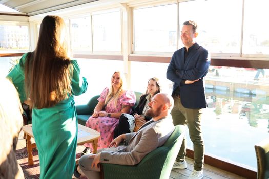A group of adults enjoy a relaxed conversation in a bright indoor setting with water views.