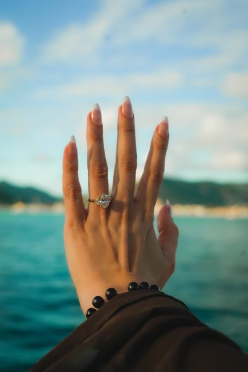 Free A female hand wearing an engagement ring with a scenic ocean background. Stock Photo