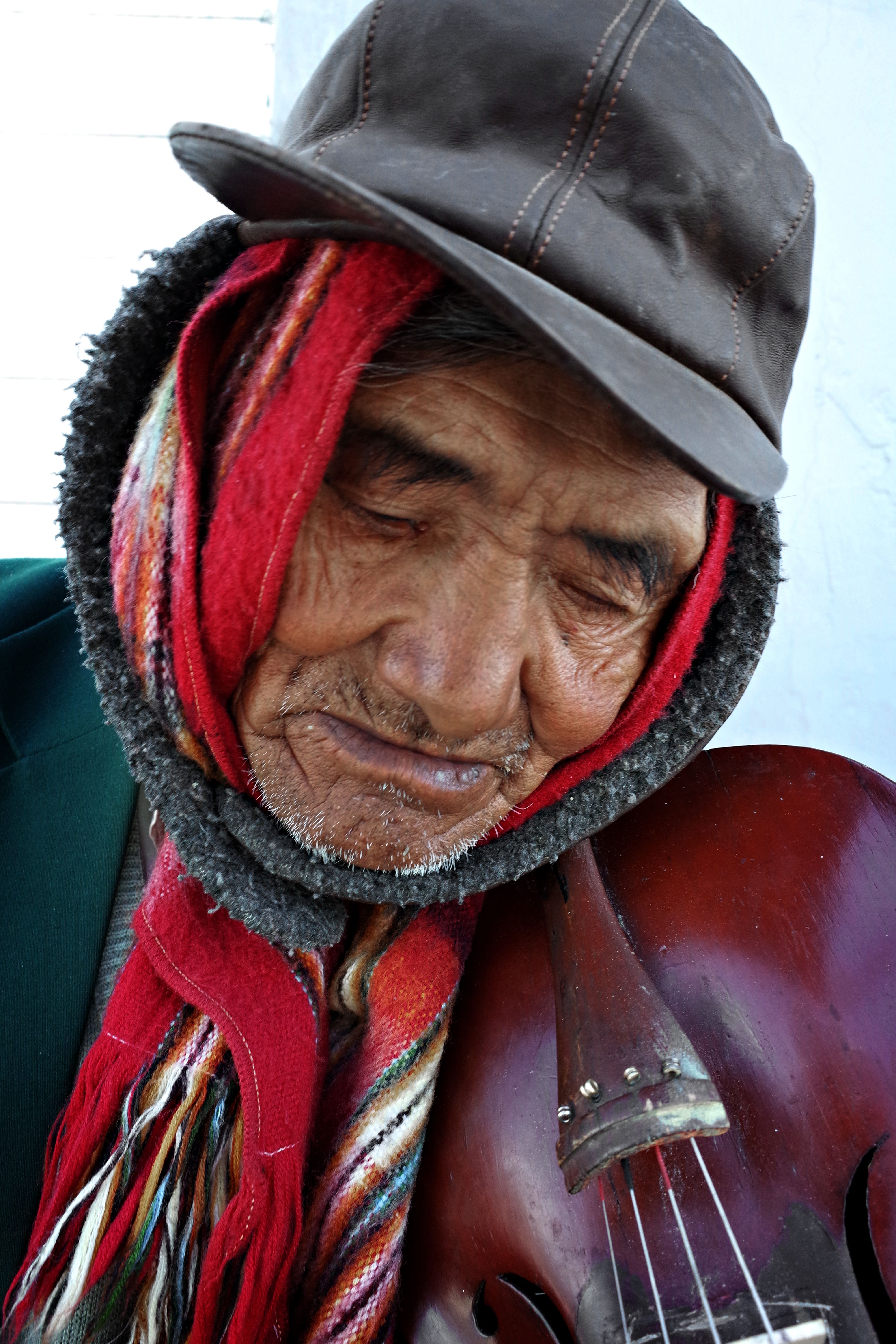Portrait of an elderly man wearing warm clothing, holding a stringed instrument closely.