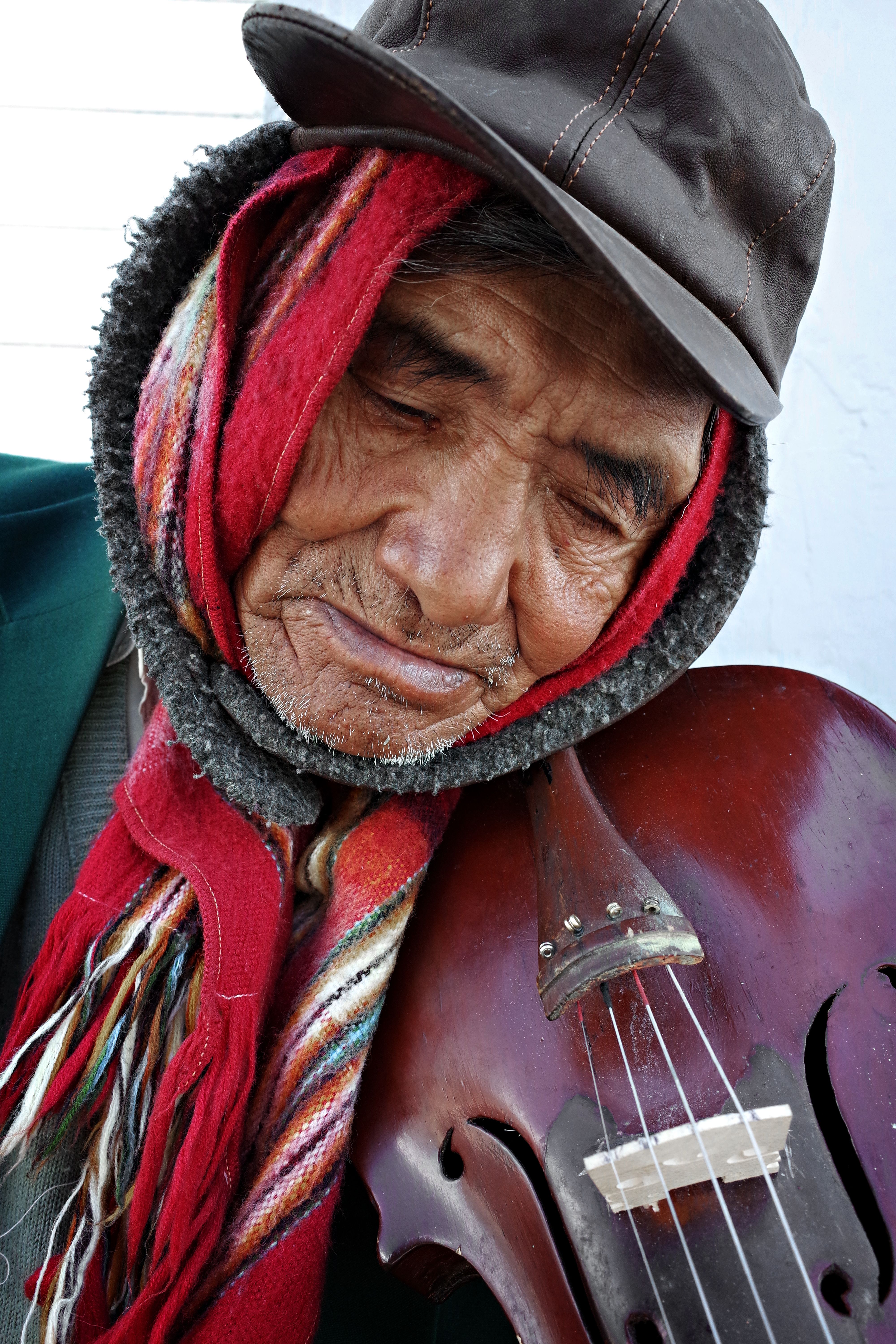 An elderly man wearing a colorful scarf embraces a violin, creating a warm, intimate moment.