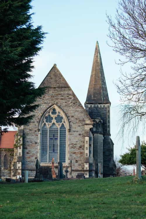 Free Charming Gothic Revival church with tall steeple and vibrant greenery on a bright day. Stock Photo