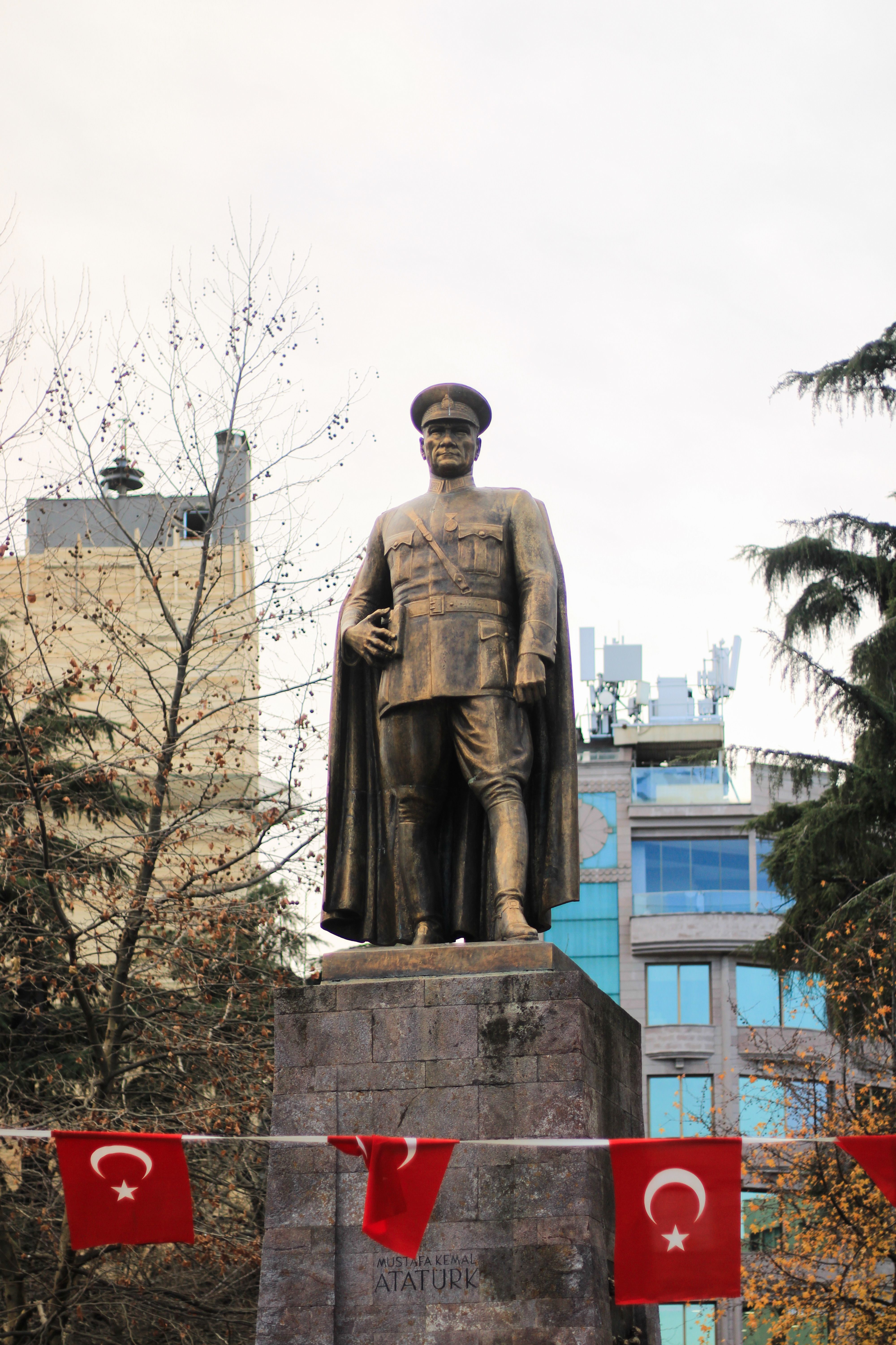 Bronze statue of Atatürk in a park in Trabzon, surrounded by Turkish flags and autumn trees.