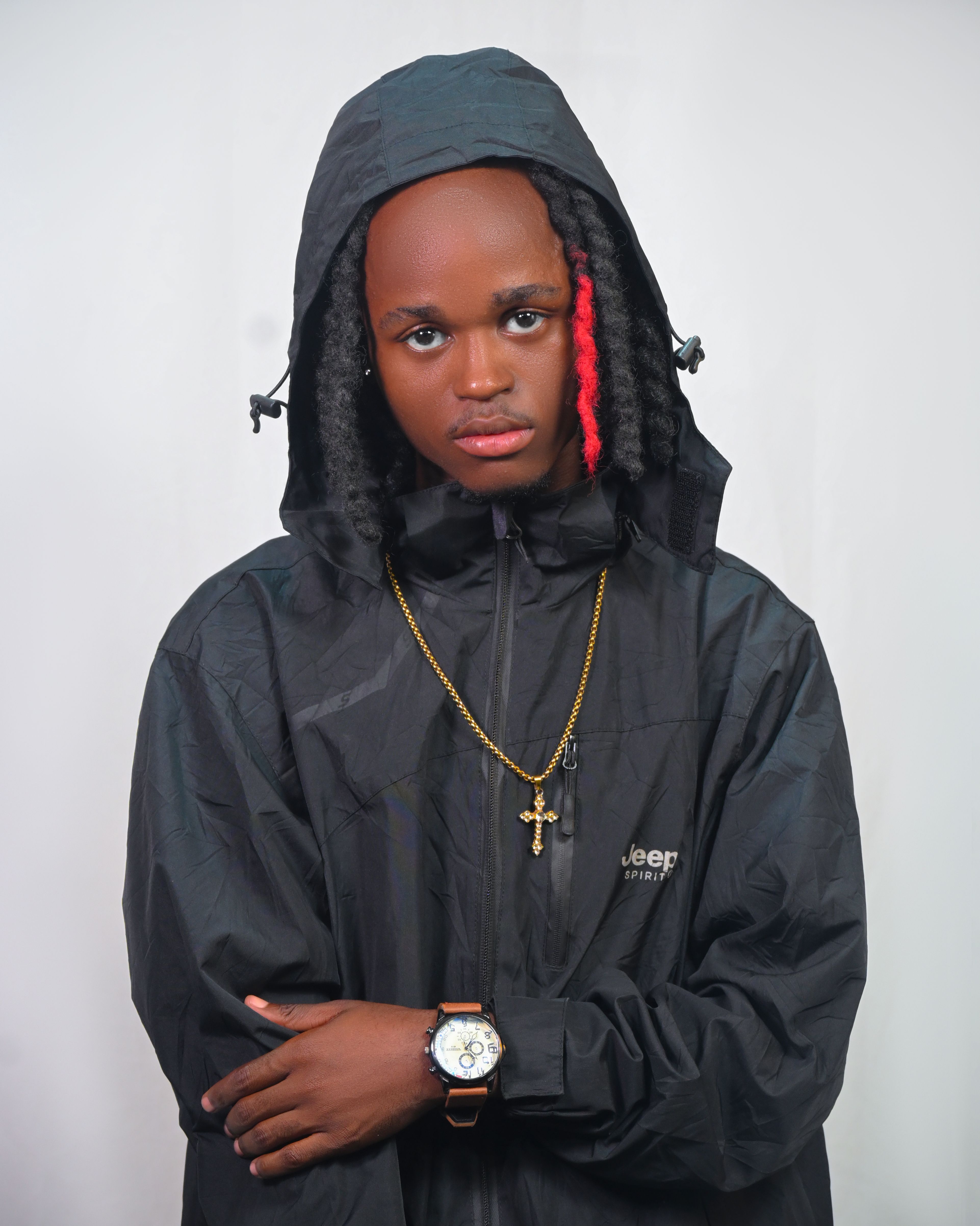 Confident young adult with braided hairstyle in a black hooded jacket and accessories.