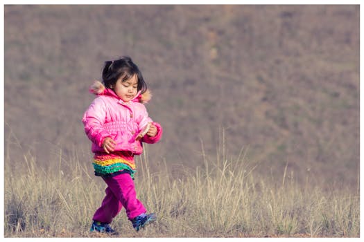 Woman in Pink Down Jacket Walking on Green Grass during Daytime