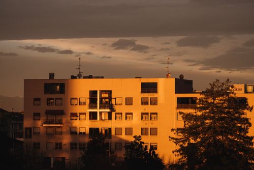 Free Golden sunlight bathes an apartment building against a moody sunset sky. Stock Photo