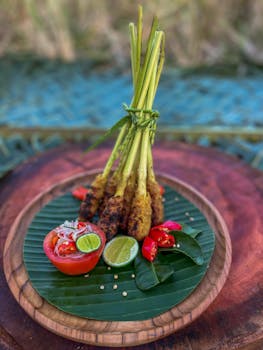 Delicious Balinese satay on banana leaves with fresh tomato and lime, showcasing Bali's culinary tradition.