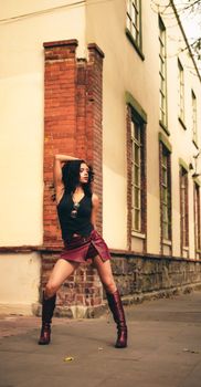 Stylish woman poses confidently in a trendy urban alley with brick walls and tall windows.