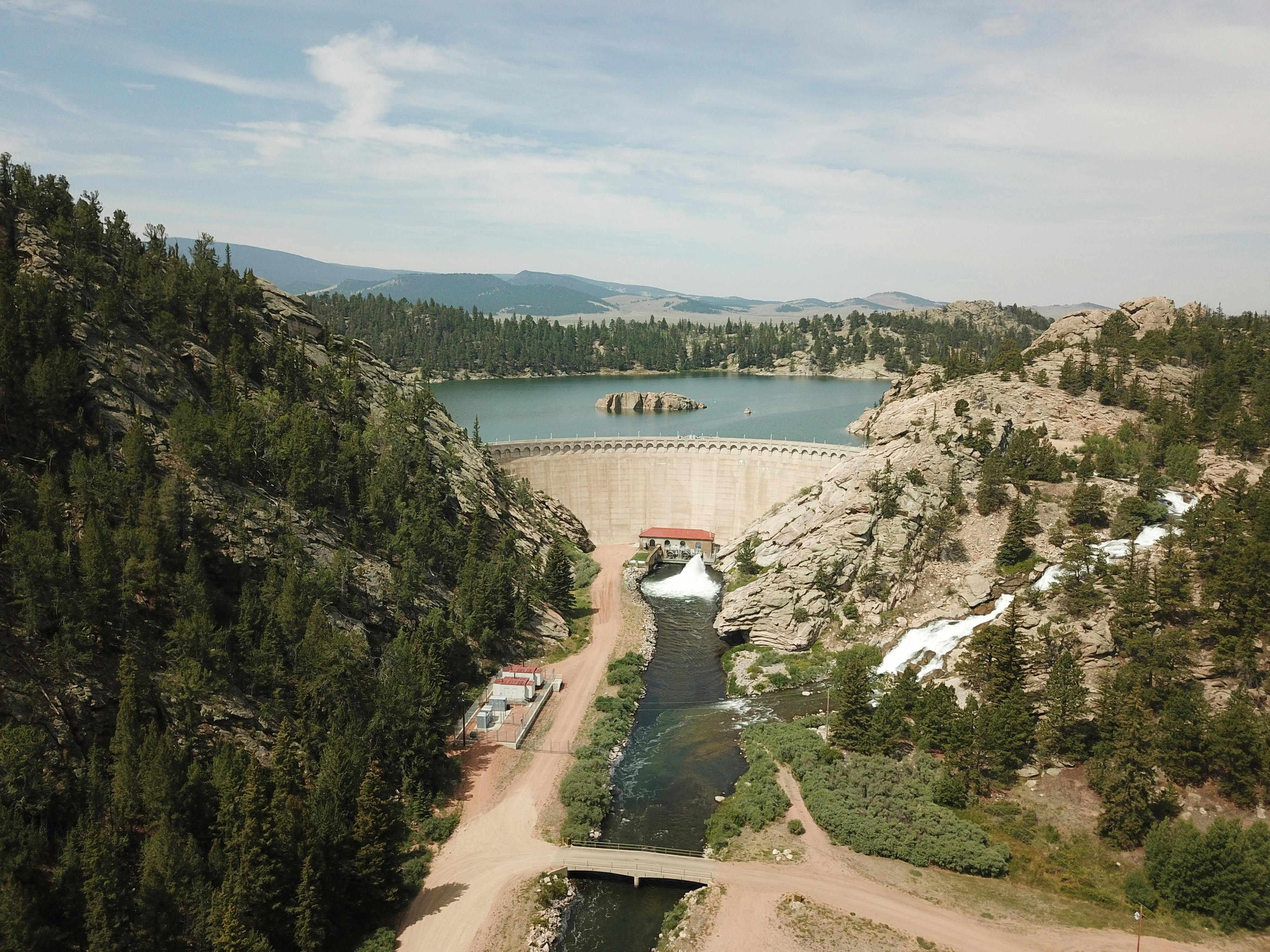 Dramatic aerial view of a dam surrounded by lush forested mountains and a vast reservoir.