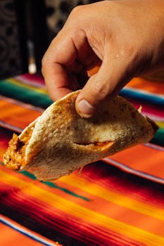 A hand holds a delicious taco against a vibrant, colorful tablecloth background.