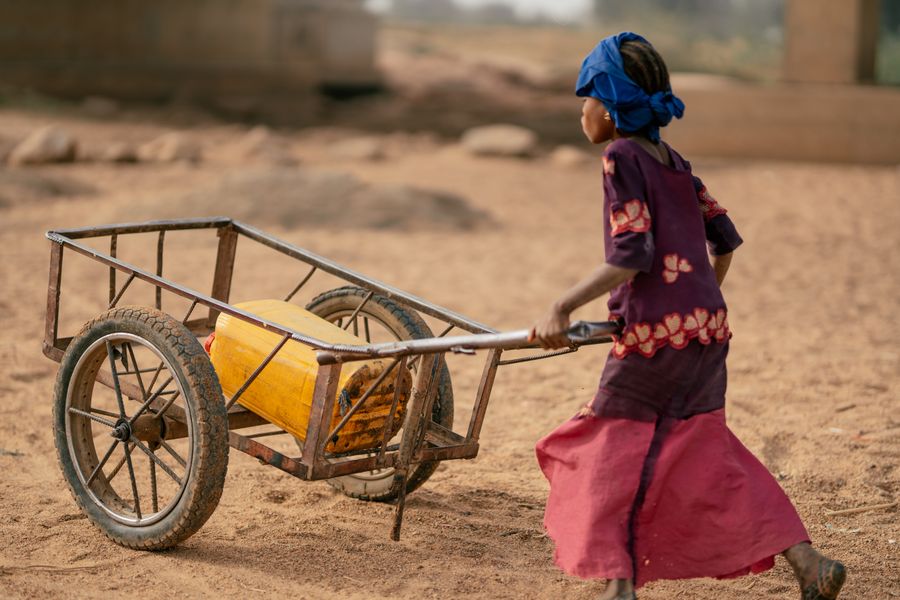 A young girl pulls a cart of water in a dry landscape