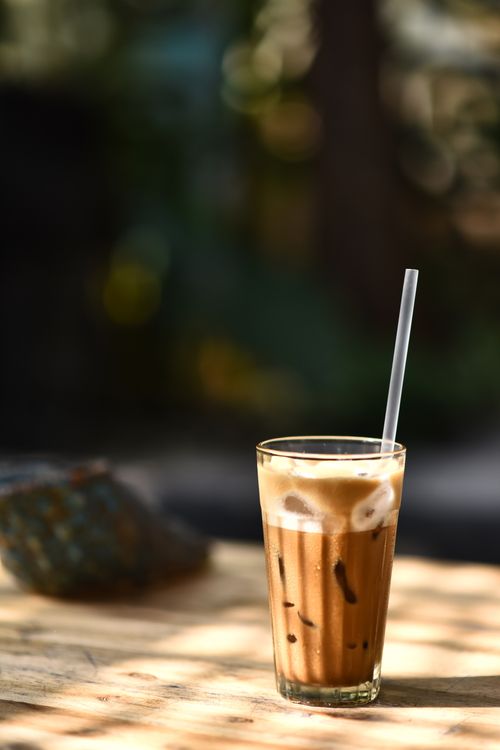 Free Chilled iced coffee with straw on a wooden table in warm outdoor sunlight. Stock Photo