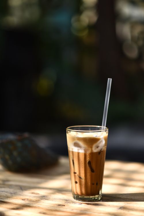 Free Glass of iced coffee with a straw on a sunlit table, outdoor setting. Stock Photo
