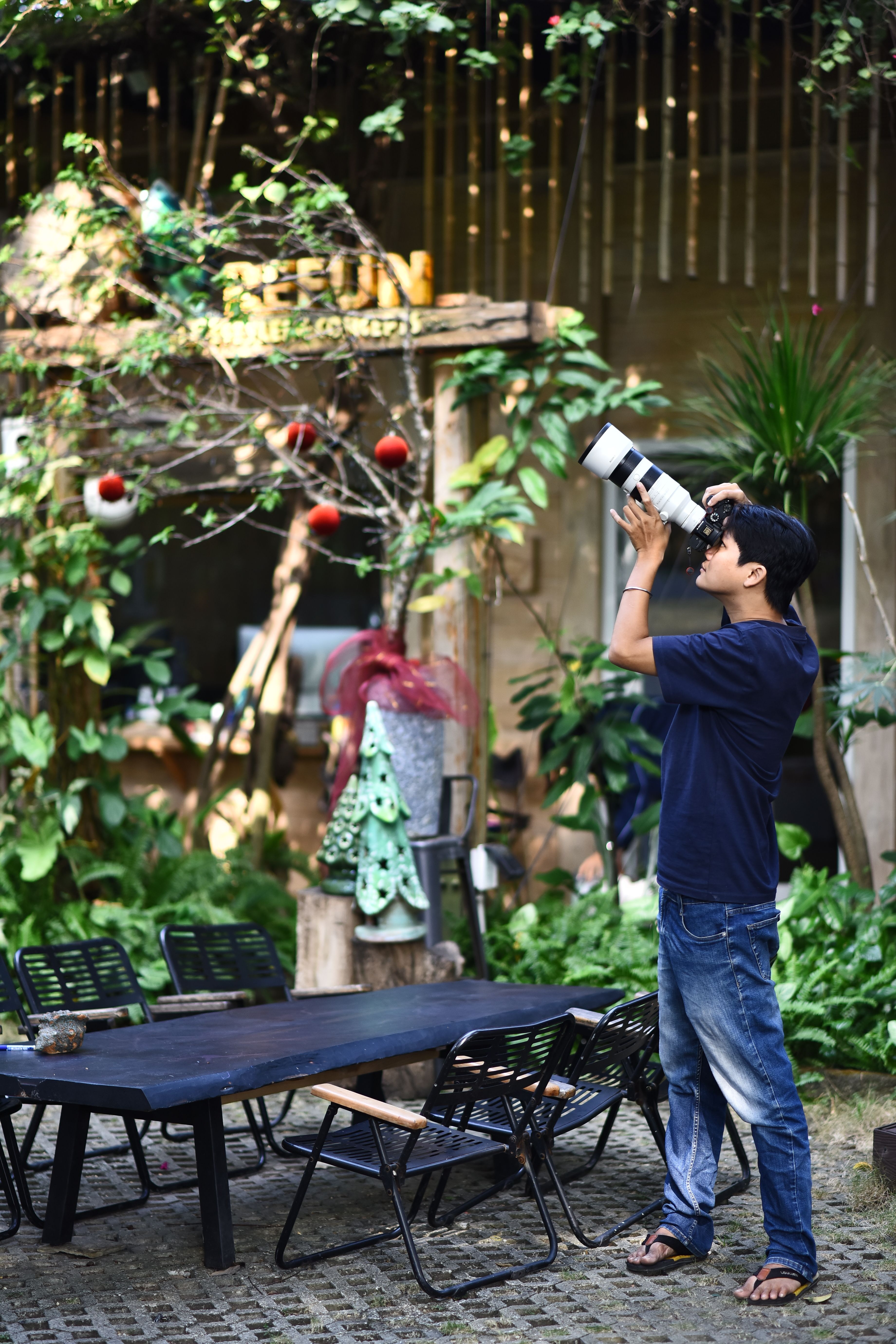 A man with a camera taking photos in a lush, outdoor café environment.