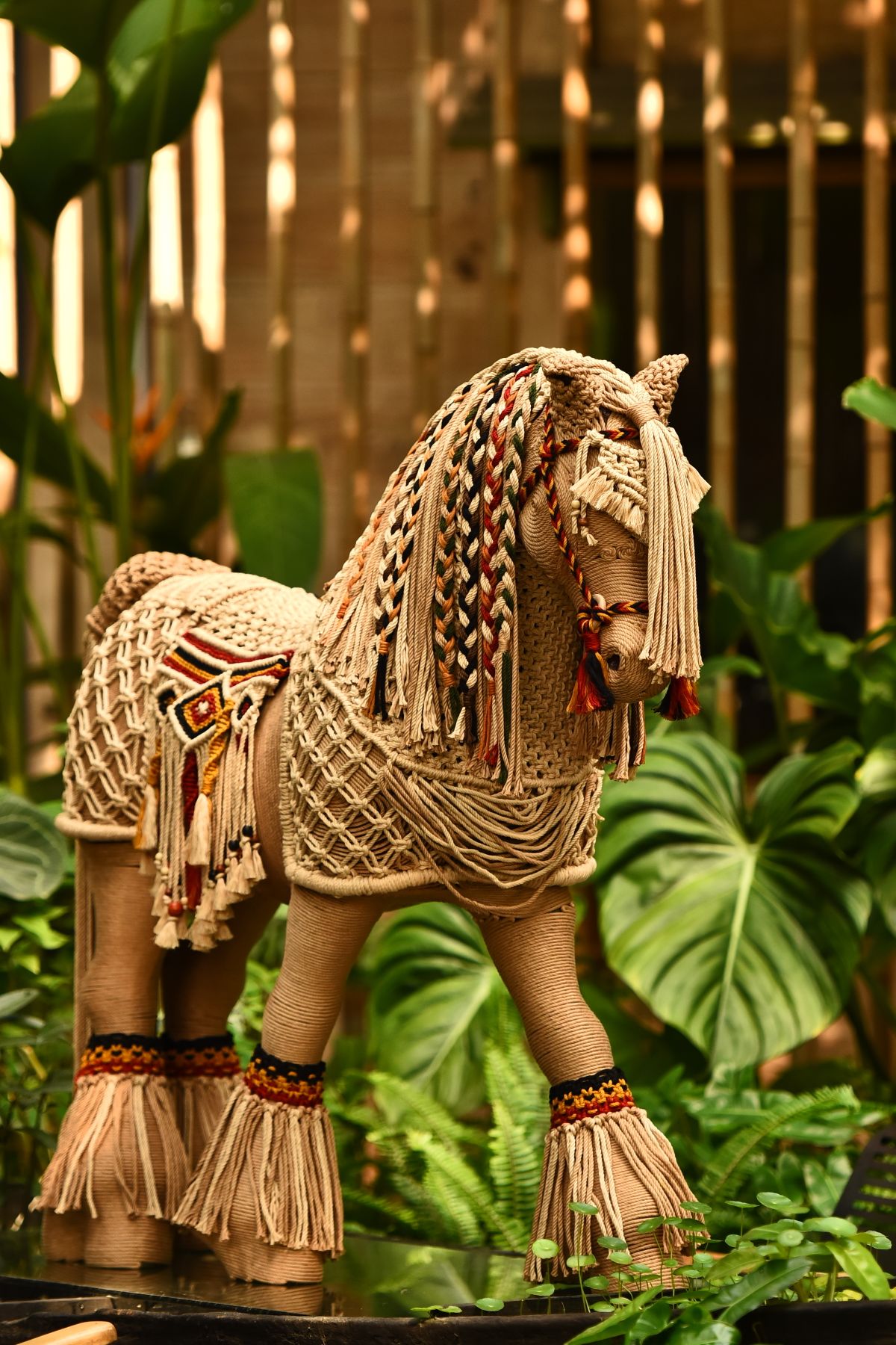 A detailed macrame horse sculpture with a flowing yarn mane among greenery