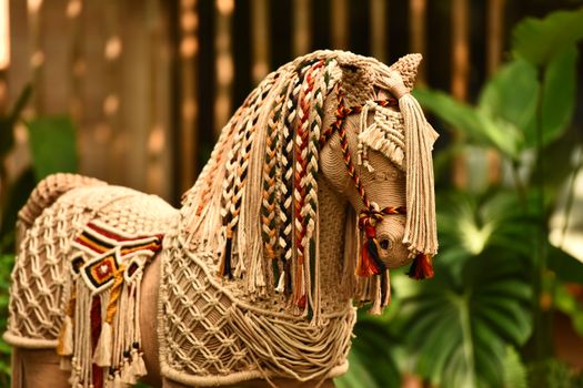 A detailed macrame horse sculpture with braided mane, set against lush greenery. Artistic and decorative.