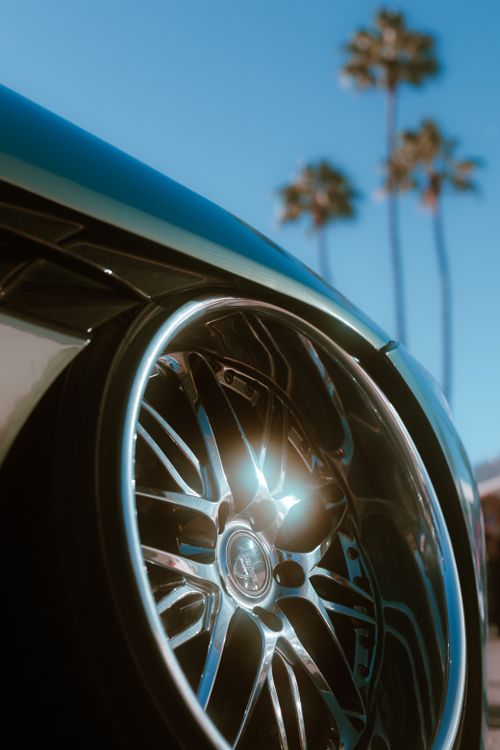 Free Close-up view of a modern car wheel with palm trees in the background under a clear blue sky. Stock Photo