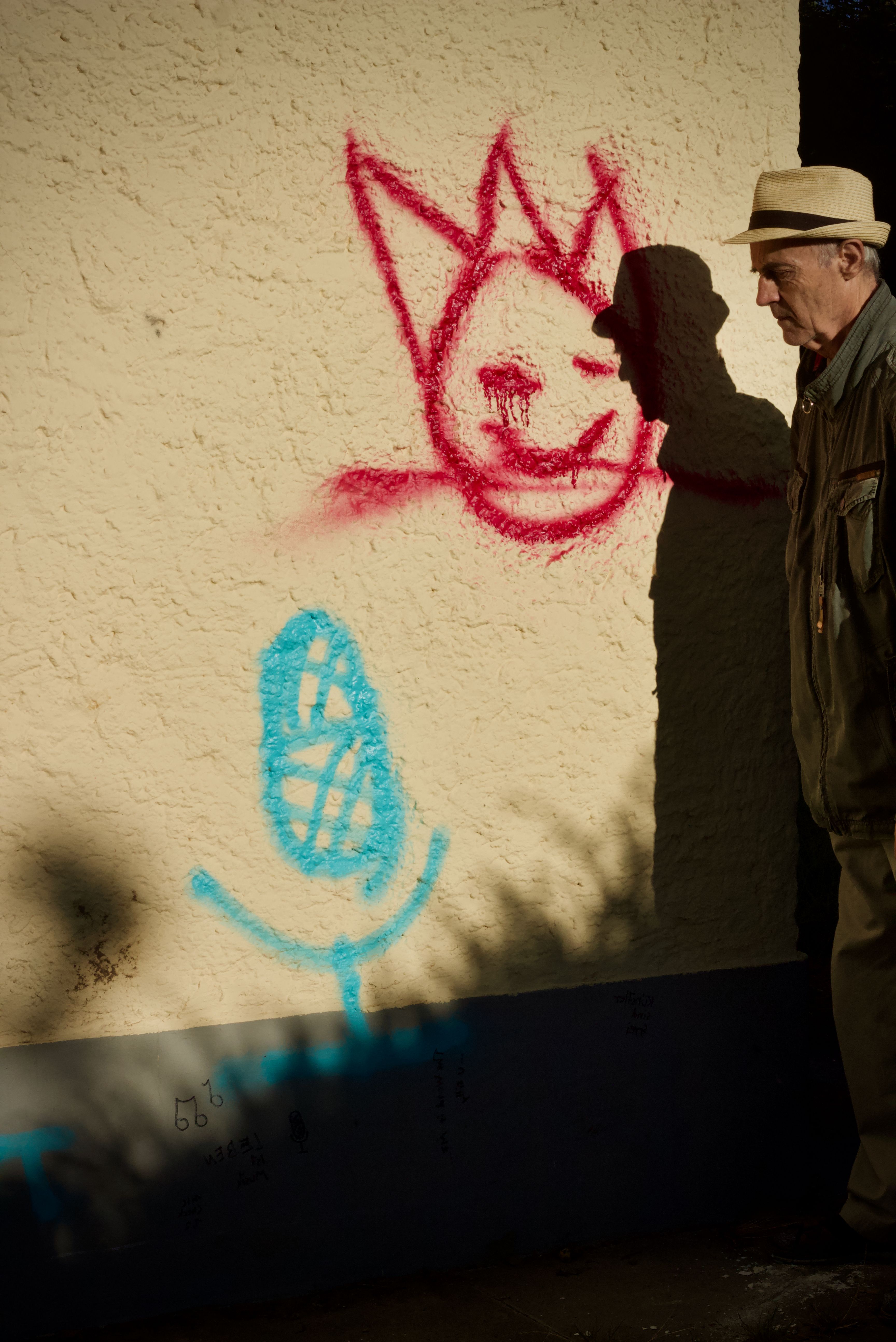 A man in a hat casts a shadow on a wall with playful graffiti.