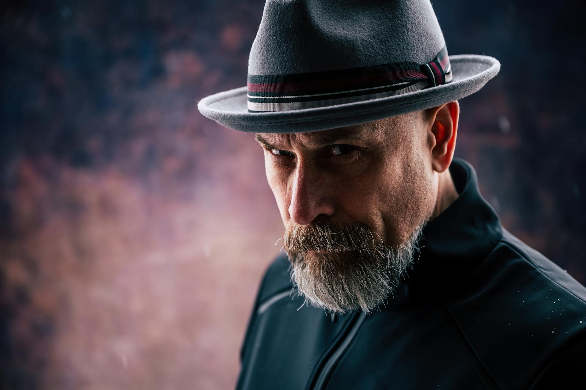 Striking close-up of a senior man with a beard wearing a fedora, exuding serious style.